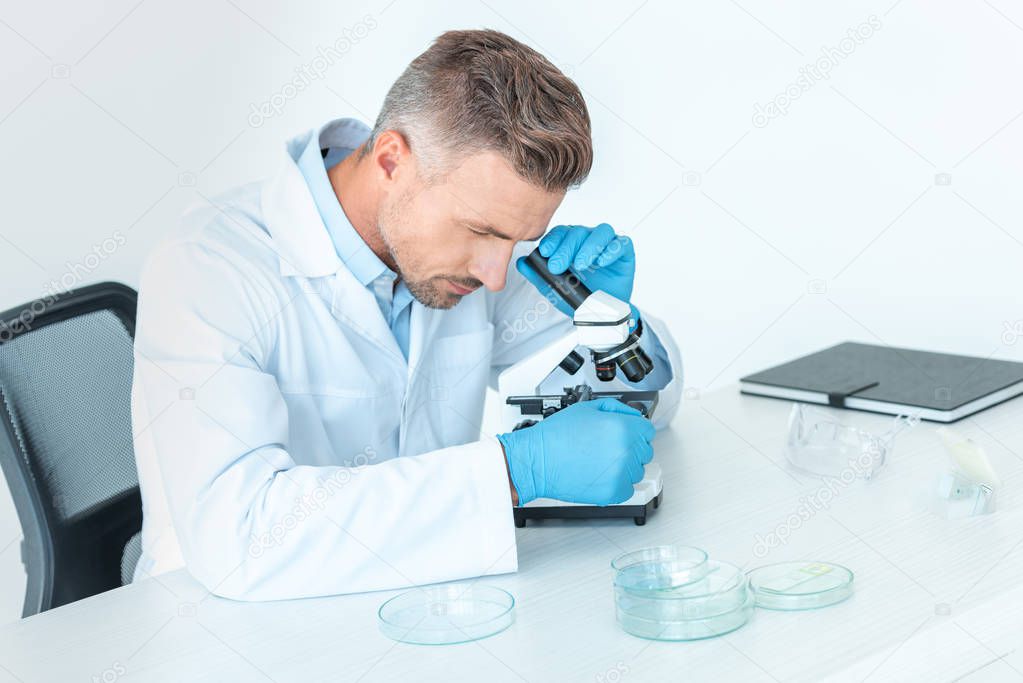 handsome chemist making test with microscope isolated on white