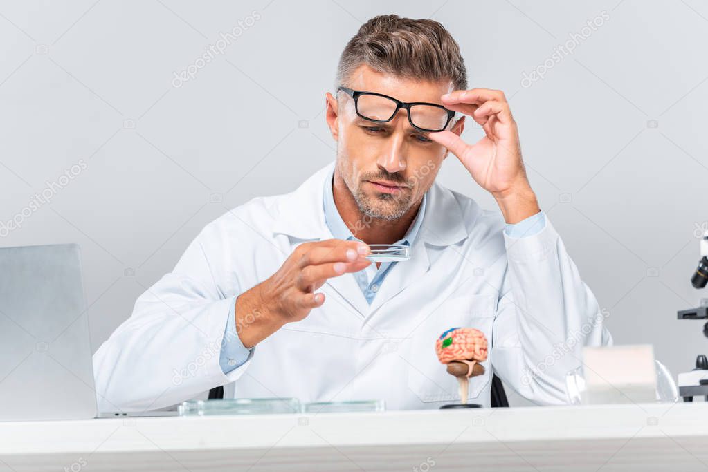 surface level of handsome scientist looking at reagent at table isolated on white