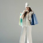 Vrolijke aantrekkelijke vrouw in stijlvolle winter trui en sjaal permanent met boodschappentassen op wit