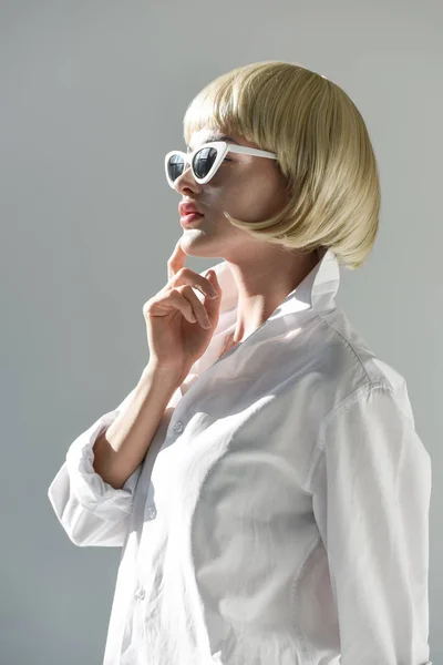 サングラスと白で隔離のあごに触れるファッショナブルな白の衣装で魅力的なブロンドの女性の側面図  — 無料ストックフォト