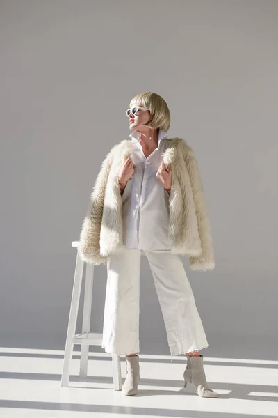 サングラスと偽ものの毛皮のコートは 白地離れて見ておしゃれな冬の服装で魅力的なブロンドの女性 — ストック写真