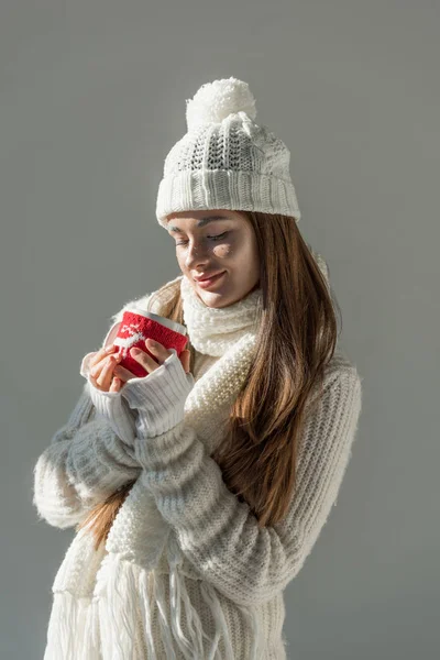 迷人的女人在时尚的冬季毛衣和围巾举行杯茶孤立在灰色 — 图库照片