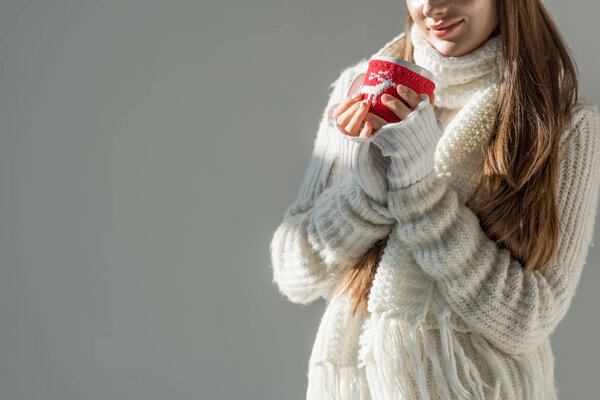 cropped image of woman in fashionable winter sweater and scarf holding cup of tea isolated on grey