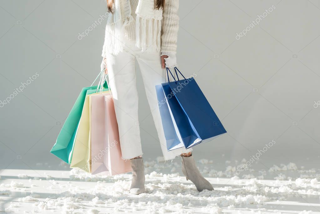 cropped image of woman in fashionable winter sweater and scarf standing with shopping bags on white