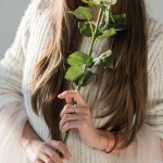 Cropped image of woman in stylish winter outfit holding white rose on white