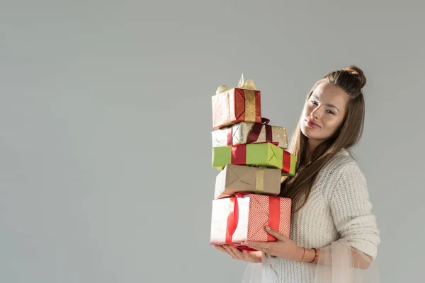 attractive woman in fashionable winter outfit holding gift boxes isolated on grey