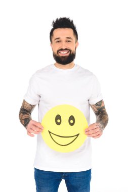 handsome bearded man with tattoos holding yellow card with happy face expression while looking at camera isolated on white clipart