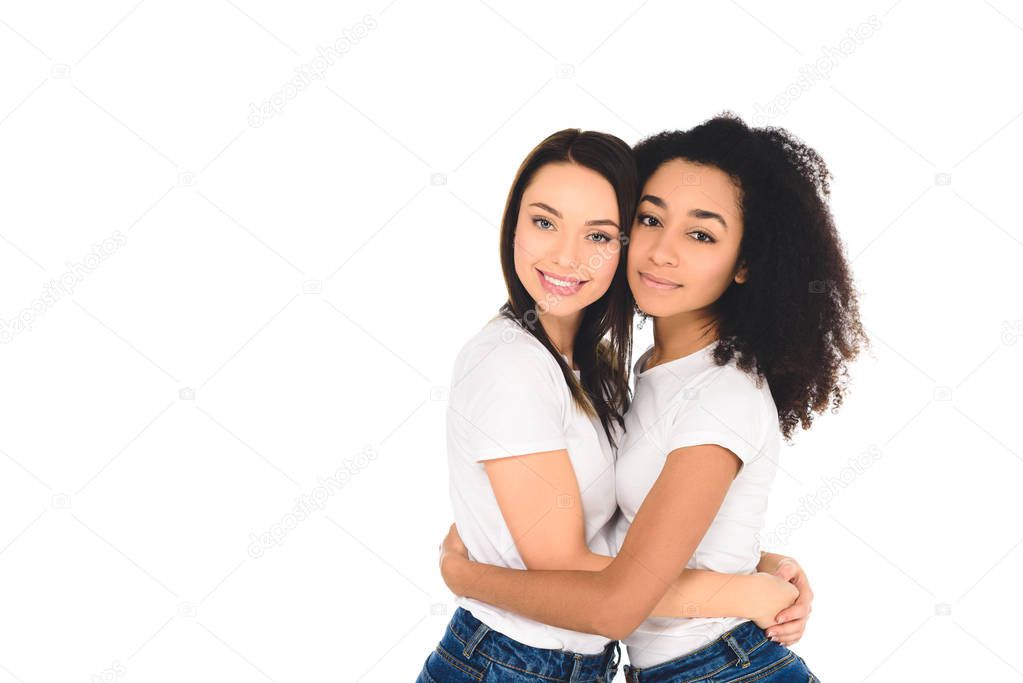 multicultural friends in white T-shirts hugging and looking at camera isolated on white