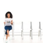 Afrikanisches amerikanisches Mädchen sitzt mit überkreuzten Beinen und Zeitung auf einem Stuhl, während sie die Kamera isoliert auf weiß betrachtet