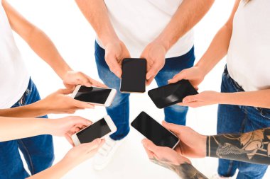 cropped view of group of people standing in circle and holding smartphones with blank screens in hands isolated on white clipart