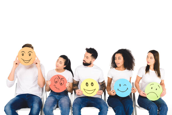 multicultural friends in white t-shirts looking at young man with cunning sign isolated on white
