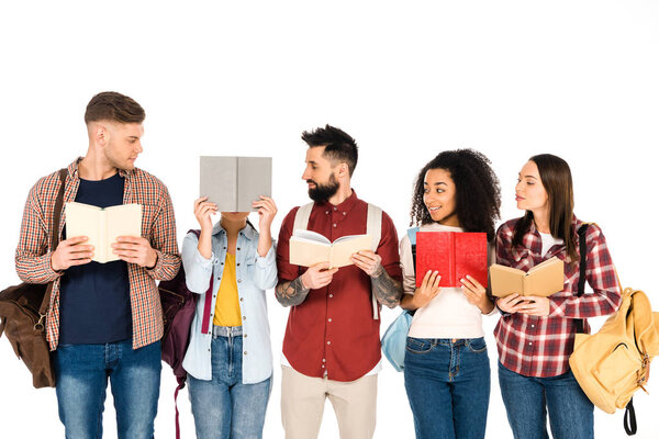 multicultural group of people holding backpacks and looking at girl with book isolated on white