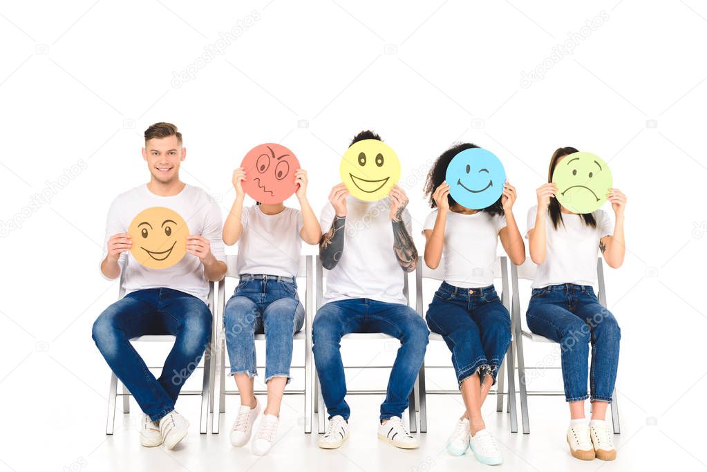 multiethnic friends in white t-shirts sitting on chairs and holding multicolored signs isolated on white