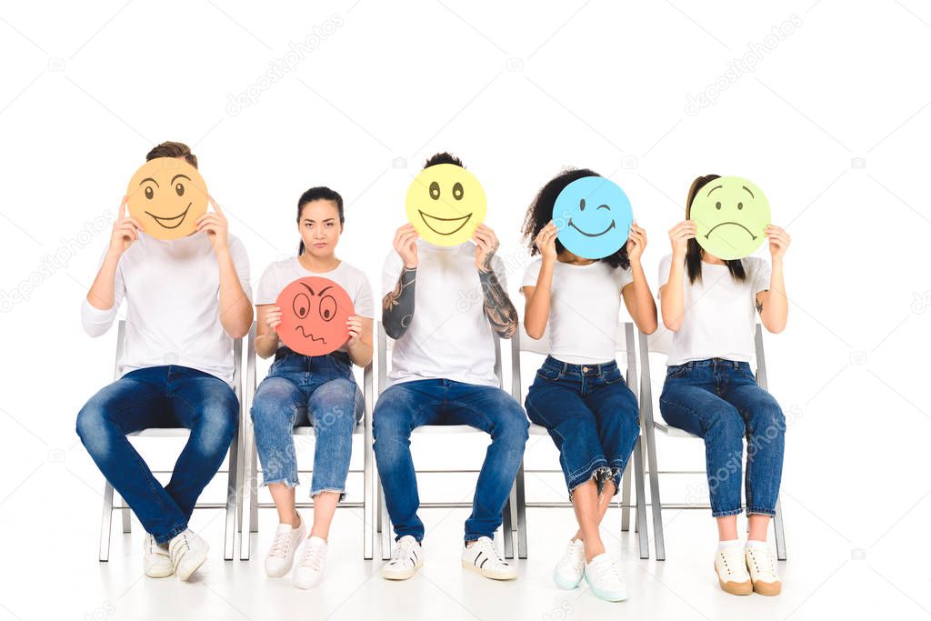 multicultural friends in white t-shirts hiding faces behind multicolored signs isolated on white