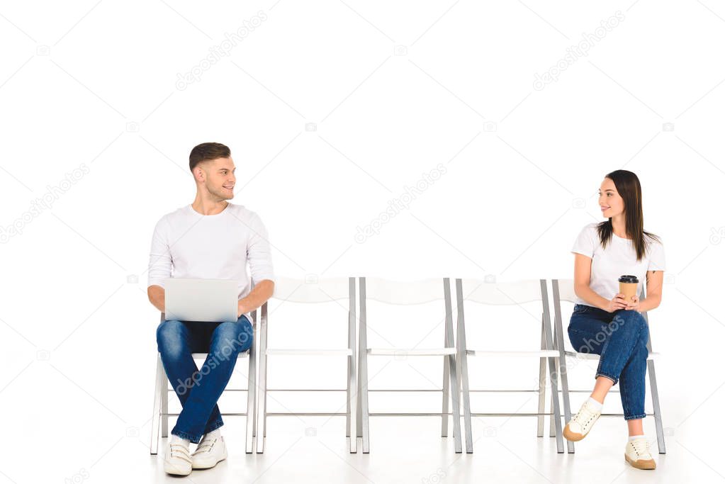 cheerful handsome man using laptop while girl holding coffee to go isolated on white