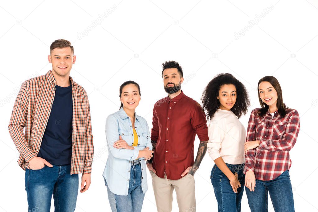 cheerful multicultural group of young people standing with crossed arms and hands in pockets isolated on white