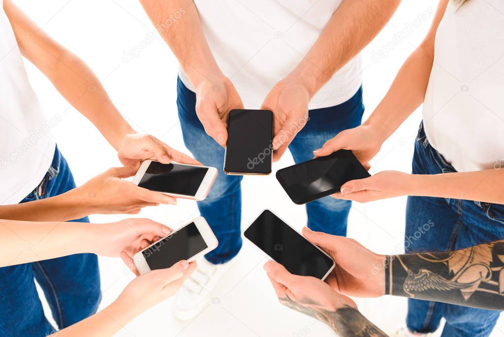 cropped view of group of people standing in circle and holding smartphones with blank screens in hands isolated on white