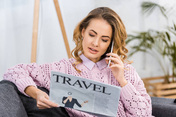 attractive woman sitting on sofa, talking on smartphone and reading travel newspaper in living room