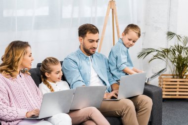mutlu aile kanepede oturan ve oturma odasında dizüstü bilgisayarlar kullanarak