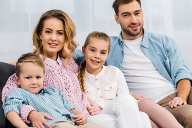happy family sitting on sofa and looking at camera in apartment clipart