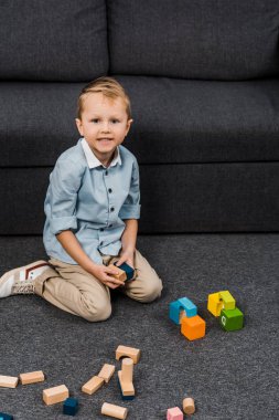 katta oturan ve kamera oturma odasında bakarak çok renkli ahşap bloklar ile boy gülümseyerek