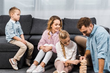 blok ahşap oynarken mutlu anne ve baba kızı oturma odasında kanepede oturan üzgün çocuk iken katta oyun kule