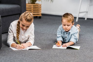 sevimli kız ve çocuk yerde yatarken ve içinde defter oturma odasında yazma