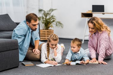 Anne kız ve yerde yatarken ve daire egzersiz kitaplarda yazılı çocuk bakarak