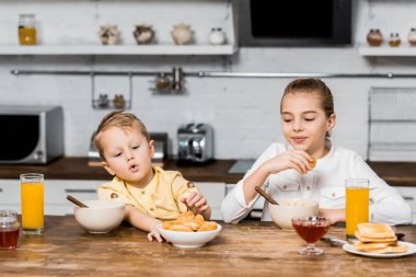 cute siblings sitting at table and holding cookies clipart