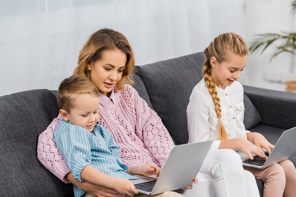 attractive woman with children sitting on sofa and using laptops in living room