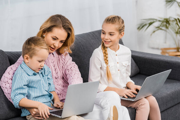 pretty woman and cute siblings sitting on sofa and using laptops in living room