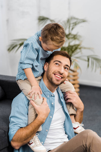 smiling boy sitting on shoulders of father in living room