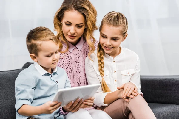 きれいな女性とソファの上に座って リビング ルームでかわいい男の子のデジタル タブレットの画面を見て微笑んでいる女の子  — 無料ストックフォト