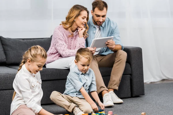 Pais Sentados Sofá Usando Tablet Digital Enquanto Crianças Brincando Com — Fotografia de Stock
