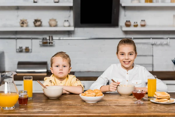 Bonitos Hermanos Mirando Cámara Sentados Mesa Con Galletas Tostadas Tazones — Foto de stock gratis