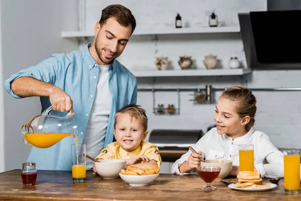 Sonriente Padre Vertiendo Jugo Naranja Vaso Mientras Los Niños Comen — Foto de Stock