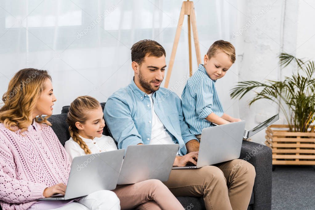 happy family sitting on sofa and using laptops in living room