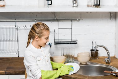 cute girl in rubber gloves washing dishes in kitchen clipart