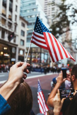 partial view of man holding american flag during parade on street in new york, usa clipart