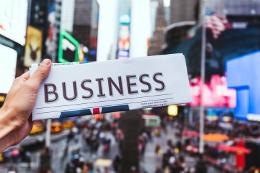 partial view of man holding business newspaper with blurry new york city street view on background clipart