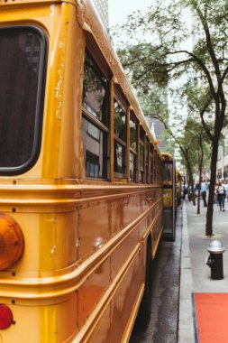 urban scene of parked yellow school buses on street in new york, usa clipart