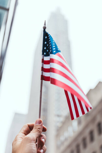 cropped shot of man holding american flag in hand with blurred new york city street on background