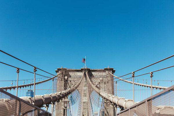 brooklyn bridge with american flag on clear blue sky background, new york, usa