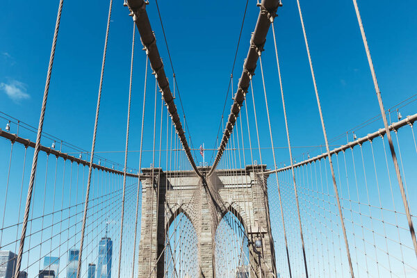 Brooklyn bridge with american flag on clear blue sky and manhattan on background, new york, usa