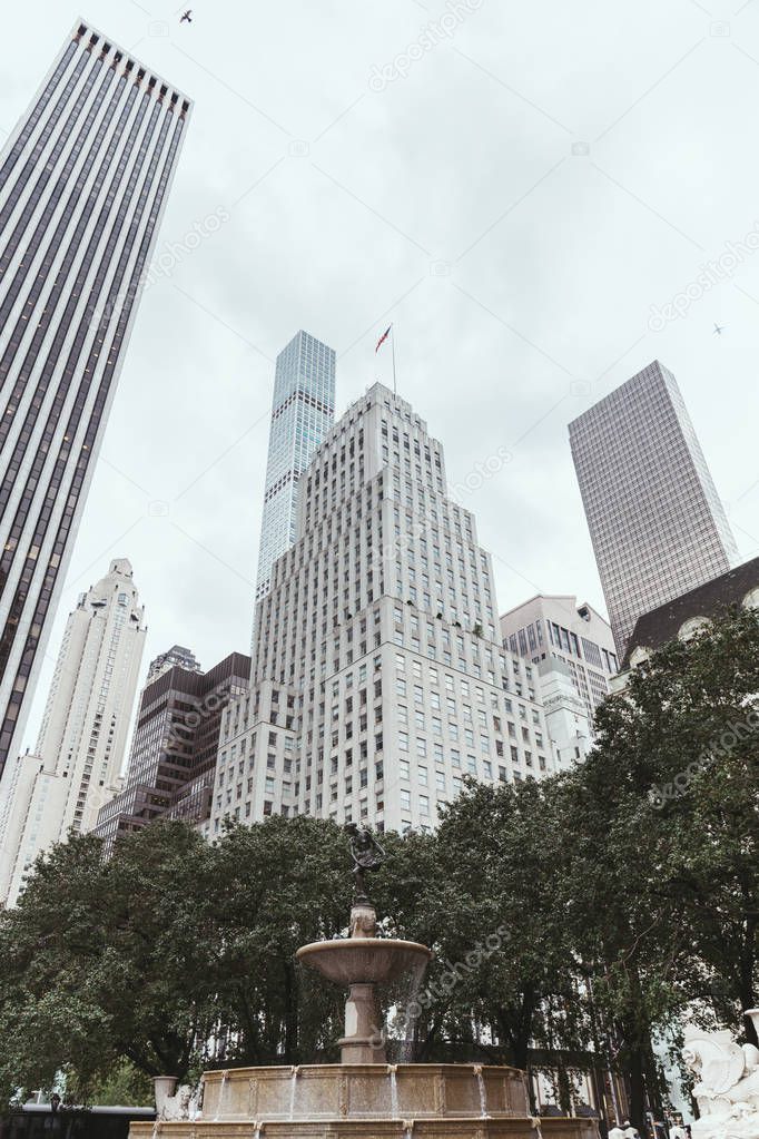 low angle view of skyscrapers, trees and city fountain in new york, usa