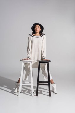 çekici Afro-Amerikan kız moda giysiler ve beyaz üzerine siyah ve beyaz sandalyelere eğilerek şapka