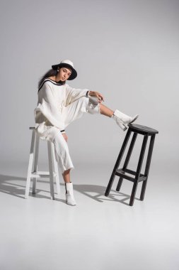 Beyaz Modern giyimleri ve beyaz sandalyede oturan ve kameraya beyaz üzerinde seyir şapka çekici Afro-Amerikan modelinde