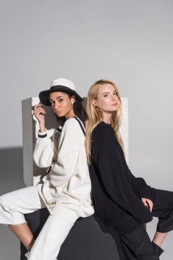 siyah ve beyaz giyimleri sırt sırta ve görünümlü kamera beyaz üzerine oturan çekici çok kültürlü kadınlar yan görünüm