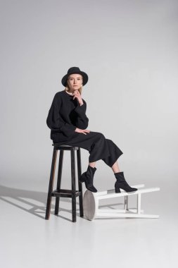 güzel beyaz sarışın kadın siyah giysiler ve sandalyede oturan ve kameraya beyaz üzerinde seyir şapka