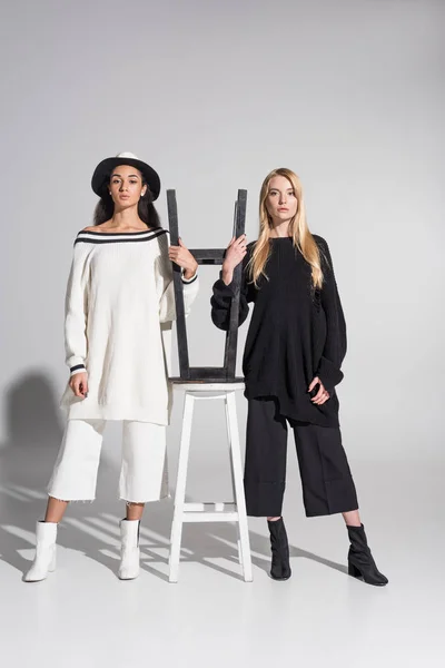 Όμορφες Πολυπολιτισμική Γυναίκες Μαύρα Και Άσπρα Ρούχα Στέκεται Κοντά Καρέκλες — Δωρεάν Φωτογραφία